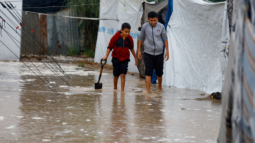 Displaced Palestinians walk through rainwater as they shelter in a flooded tent camp on a rainy day in Nuseirat, central Gaza Strip, December 12, 2025. REUTERS/Mahmoud Issa
