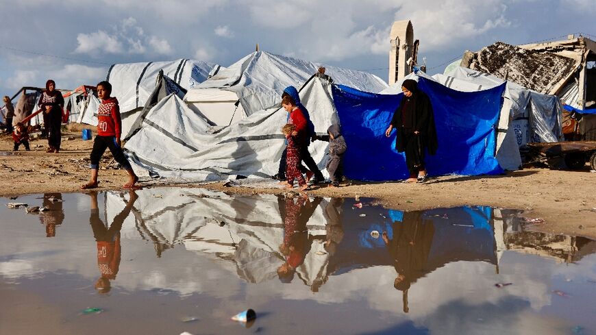 Displaced Palestinians walk past a large pool of standing water in Gaza City. Heavy winter rains have have made an already precarious life worse for displaced Gazans