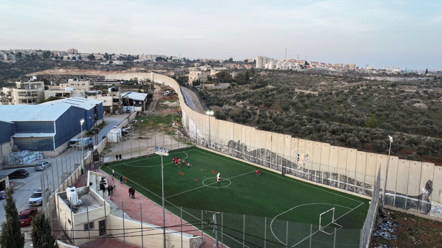Drone view shows a man dressed as Santa playing football with Palestinian teens next to West Bank barrier separating Aida refugee camp from Jerusalem, in the Israeli-occupied city of Bethlehem, December 22, 2025. REUTERS/Ammar Awad