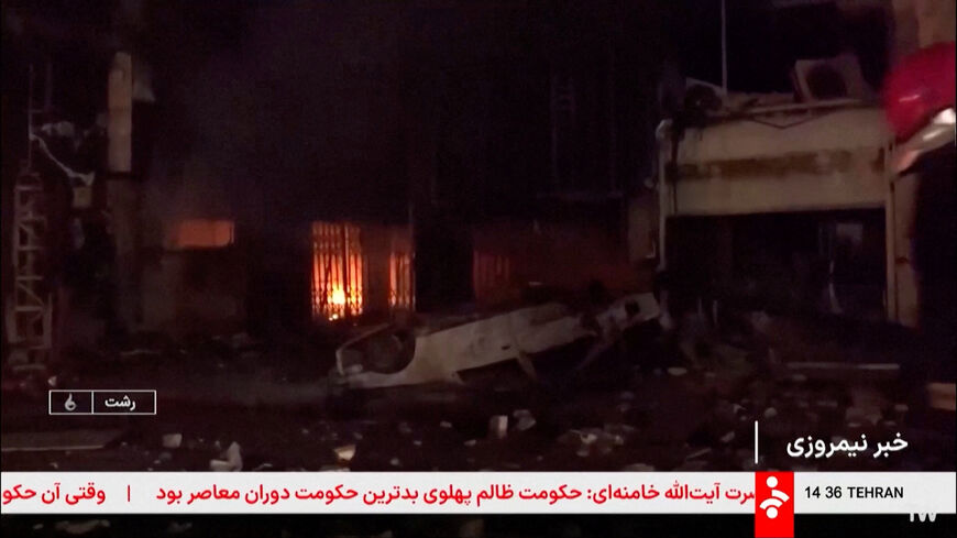 A damaged car lies outside a burning building following unrest sparked by dire economic conditions, in a place given as Rasht, Iran, January 9, 2026, in this screengrab from Iran's state media broadcast footage. IRIB via WANA(West Asia News Agency) via REUTERS