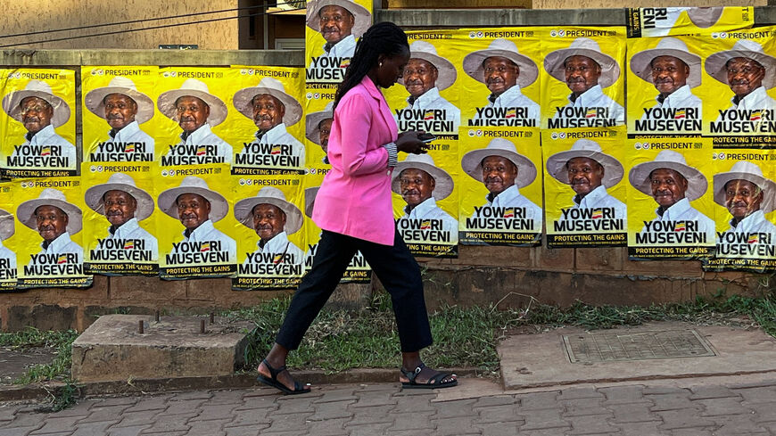 A woman uses a mobile phone as she walks past campaign posters of Yoweri Museveni, Uganda's President and presidential candidate of the ruling National Resistance Movement (NRM), ahead of the general election in Kampala, Uganda, January 14, 2026. REUTERS/Thomas Mukoya