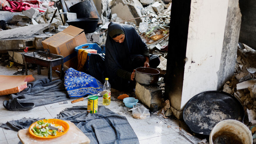 FILE PHOTO: A Palestinian woman cooks, with the rubble of residential buildings destroyed during the war visible in the background, in Jabalia, northern Gaza Strip, January 6, 2026. REUTERS/Mahmoud Issa/File Photo