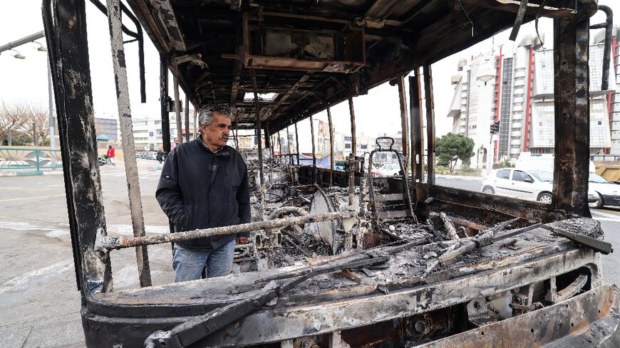 A man stands in the wreckage of a burned bus in Tehran's Sadeghieh Square on January 15, 2026