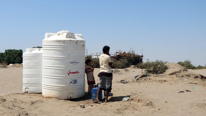 People standing next to water tanks at Al Salam camp for the internally displaced in Aden