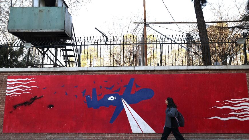 A woman walks past a mural depicting a US drone painted on the outer walls of the former US embassy in Tehran