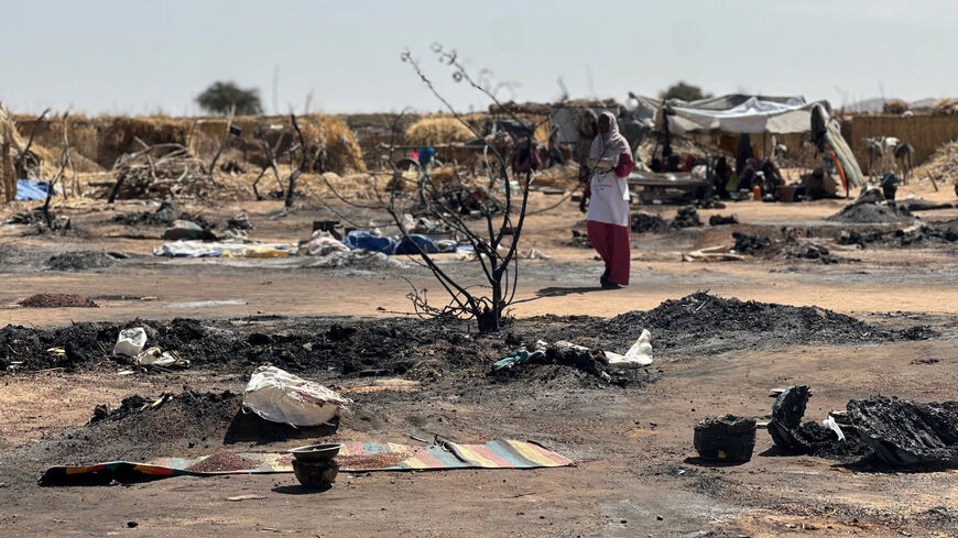 A displaced Sudanese woman who left El-Fasher after its fall with others, walks amid the remains of a fire that broke out at a camp in Tawila on Feb. 11, 2026. 