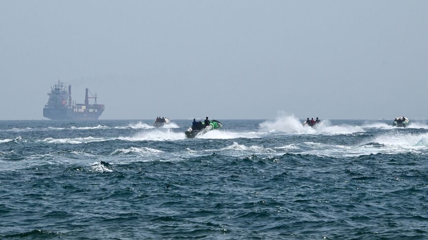 Small boats loaded with merchandise sail past the St. Kitt's and Nevis-flagged container ship Marsa Victory in the waters of the Strait of Hormuz off the coast of Khasab in Oman's northern Musandam Peninsula, on June 25, 2025.