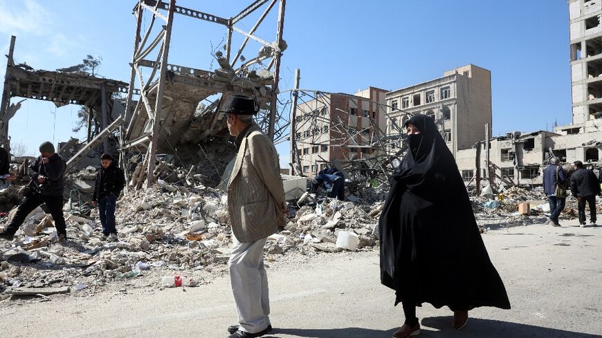 A man and a woman walk past destroyed buildings following airstrikes in central Tehran, on March 4, 2026