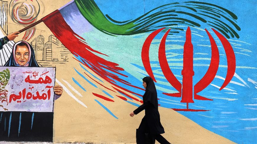 An Iranian woman walks past an anti-US and anti-Israel mural in Tehran 
