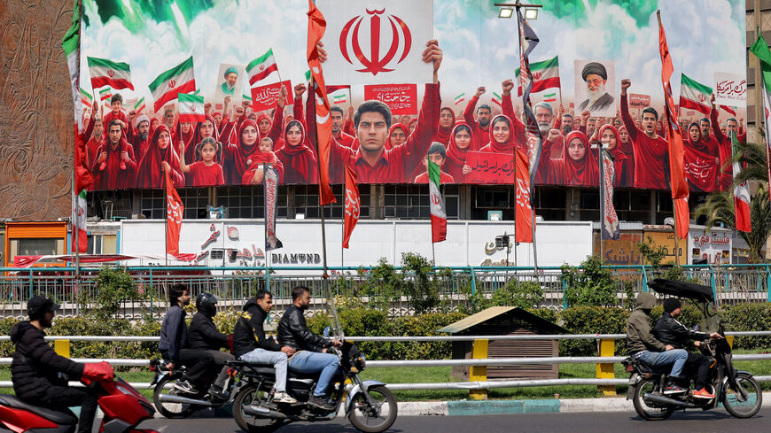 Motorists ride scooters near a large political banner, depicting missiles being fired behind Iranian demonstrators in solidarity with the government, at Valiasr Square in Tehran on April 6, 2026. 