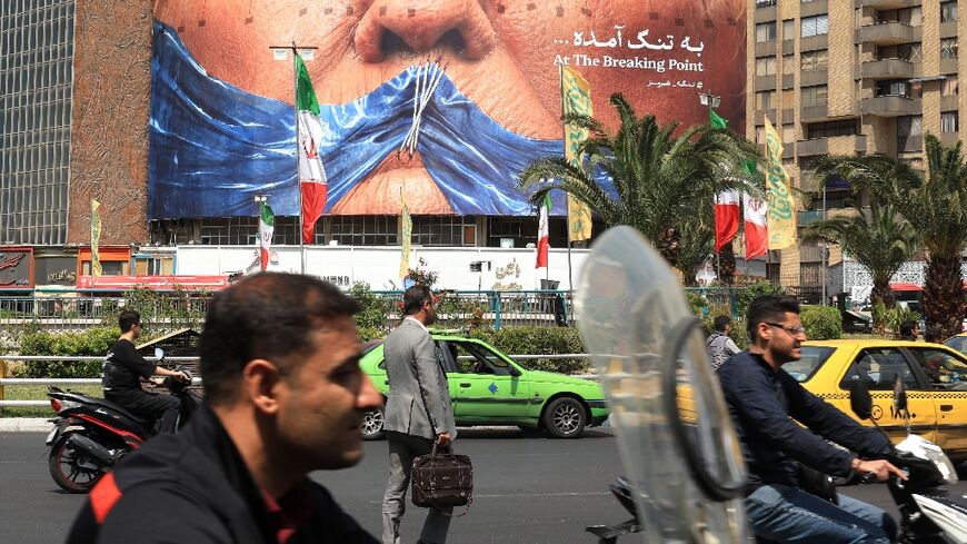 Commuters make their way past an anti-US billboard referring to President Donald Trump and the Strait of Hormuz, installed on a building at the Valiasr Square in Tehran
