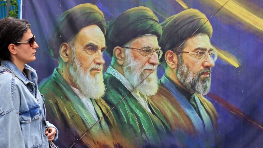 A woman walks past a banner featuring Iran's late supreme leaders, Ayatollah Ruhollah Khomeini (L) and Ayatollah Ali Khamenei (C), next to newly elected Supreme Leader Ayatollah Mojtaba Khamenei, in Tehran on April 19, 2026. 