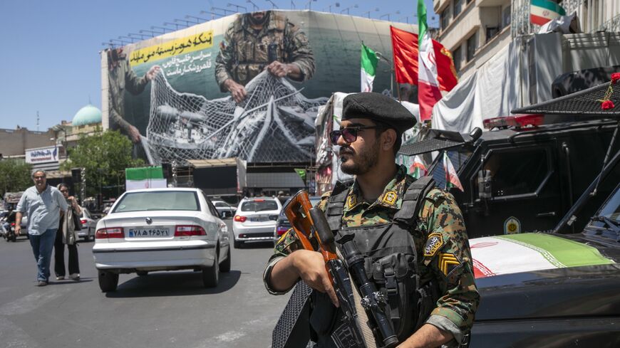 An Iranian police office stands on patrol near a poster depicting Iranian soldiers holding a net in the shape of the Strait of Hormuz, with US military aircraft ensnared in a fishing net, on May 9, 2026 in Tehran, Iran. 