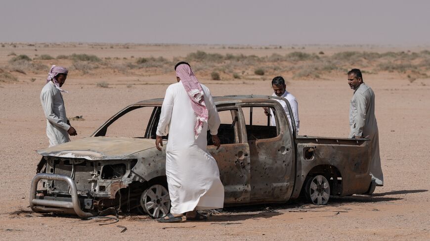 Men gather around the husk of a destroyed pickup truck that was driven by a local shepherd who was reportedly struck by Israeli forces and buried by locals at a grave nearby, in the Najaf desert in southwestern Iraq, on May 12, 2026. 
