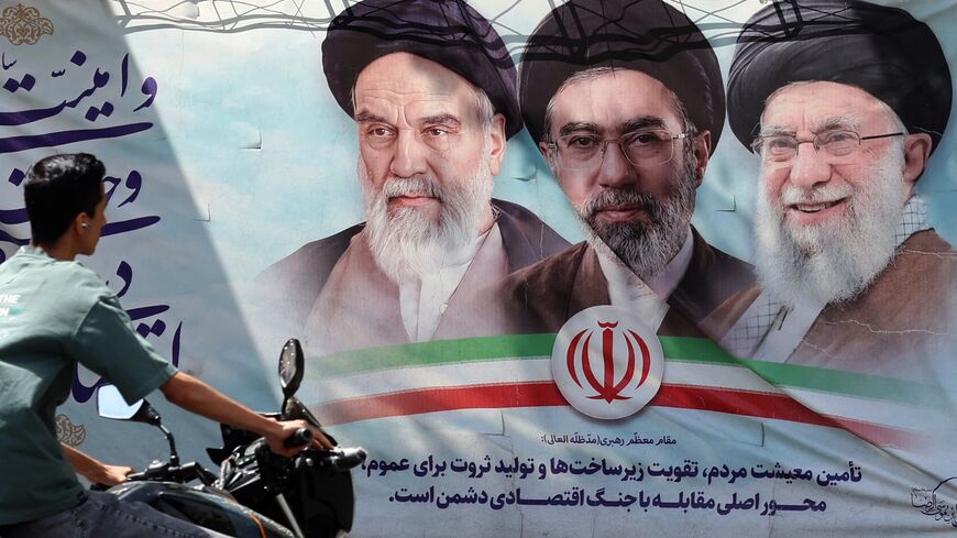 An Iranian man rides his motorbike past a billboard on May 28, 2026.
