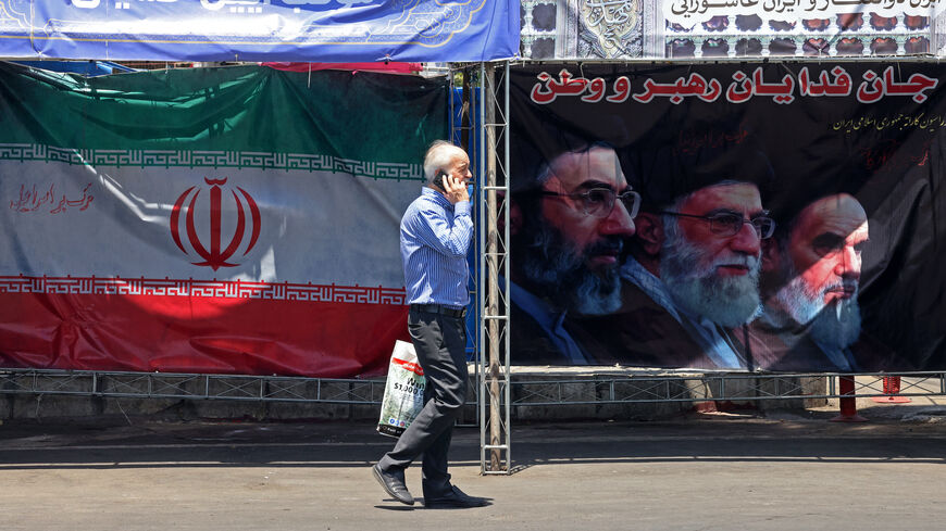 A man walks past Iran's national flag and a banner bearing the images of the late founder of the Islamic Revolution supreme leader Ayatollah Ruhollah Khomeini (R), the late Iranian supreme leader Ali Khamenei and his son, the current supreme leader Mojtaba Khamenei (L), erected along a street at the Vanak Square in Tehran on June 10, 2026.
