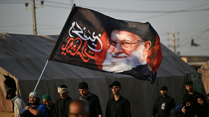 Shiite Muslim pilgrims hold a flag bearing the portrait of Iran's slain supreme leader Ayatollah Ali Khamenei
