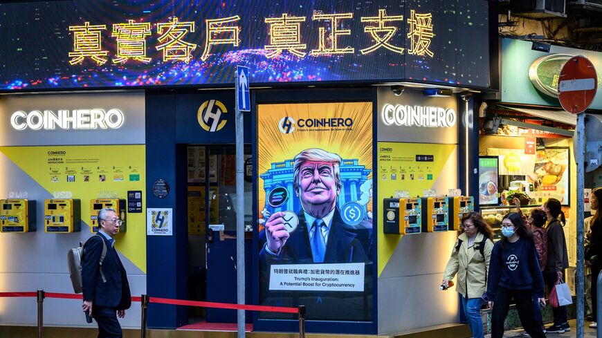 People walk past a cryptocurrency exchange office with a screen featuring US President Donald Trump holding cryptocurrency coins in Hong Kong on March 12, 2025.