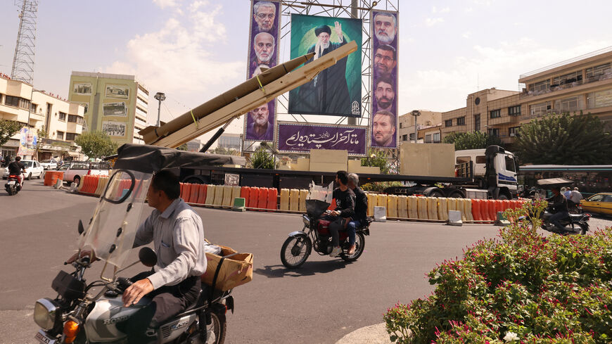 Iranians ride their motorcycles past a deactivated Kheibar Shekan ballistic missile in front of a picture of Iran's Supreme Leader Ayatollah Ali Khamenei in Tehran's Bahrestan Square on September 27, 2025, as part of an exhibit to mark the "Sacred Defense Week" commemorating the 1980-88 Iran-Iraq war. (Photo by ATTA KENARE / AFP) (Photo by ATTA KENARE/AFP via Getty Images)
