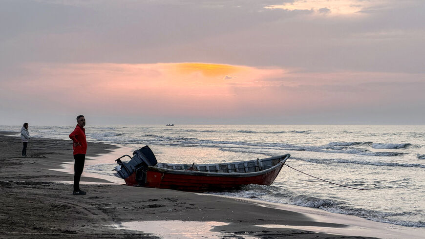 A man stands near a boat moored along a beach on the Caspian Sea coast in Sorkhrud in Iran's northern Mazandaran province on March 24, 2026, where many families have relocated due to the ongoing war with the US and Israel. Israel and the United States launched strikes on Iran on February 28, killing the Islamic republic's supreme leader and sparking a war that has since spread across the Middle East. (Photo by ATTA KENARE / AFP via Getty Images) /
