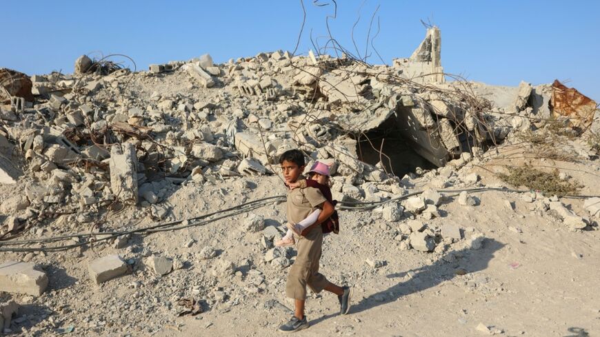 A Palestinian child carries a little girl on his back as he walks past the rubble of destroyed buildings in the Jabalia camp for Palestinian refugees in the northern Gaza Strip