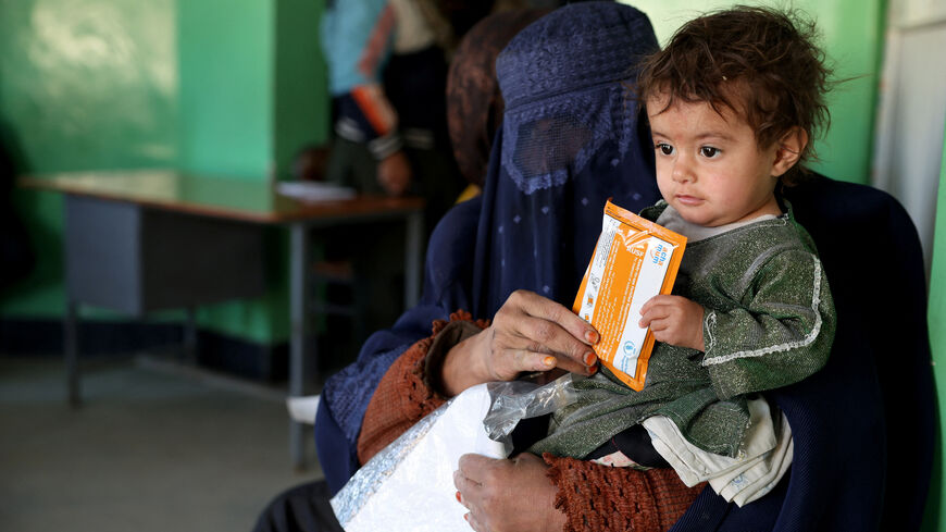 Halima, 40, holds her child with a sachet of Plumpy’Nut, while sitting on a bench at the WFP-supported Qasaba Clinic after an increase in malnutrition cases following the return of deported Afghans, in Kabul, Afghanistan, January 7, 2026. REUTERS/Sayed Hassib