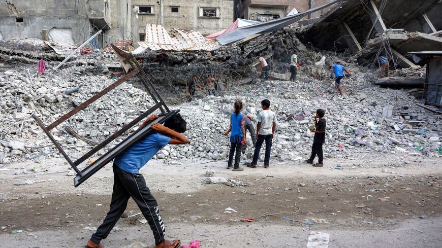 A boy walks carrying a table on his back past salvage workers scrapping the rubble of a building that was destroyed during Israel's war against Hamas in Gaza City on Aug. 16, 2026. — Photo by Omar Al-Qattaa / AFP via Getty Images