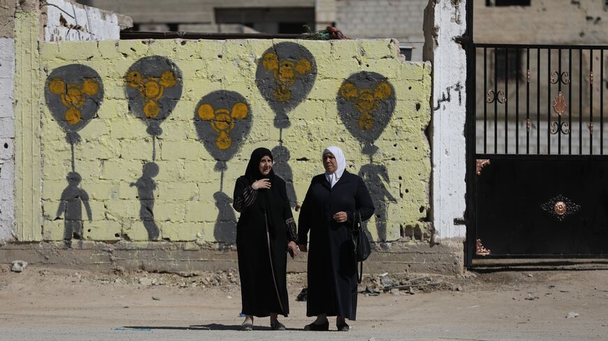 Two women stand before graffiti on the cemetery wall for victims of the chemical massacre, on Aug. 21, 2025 in Zamalka, Syria. 