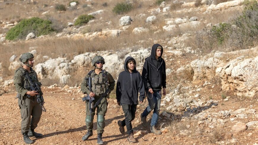 Israeli soldiers look on as settlers walk along a dirt road where Palestinian farmers are harvesting their olive trees in the West Bank village of Deir Abu Mashal