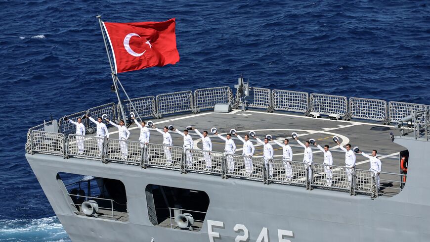 Turkish Navy sailors wave their caps from the flight deck 