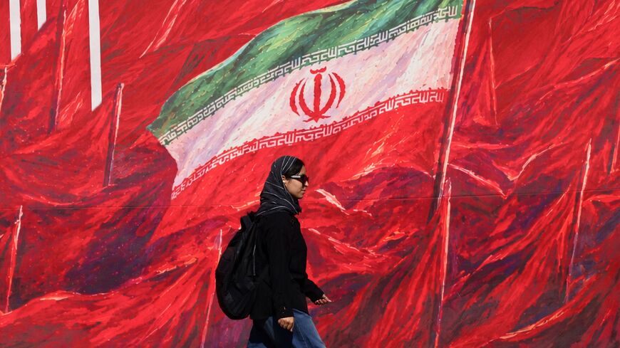 A woman walks past a mural bearing the Iranian national flag