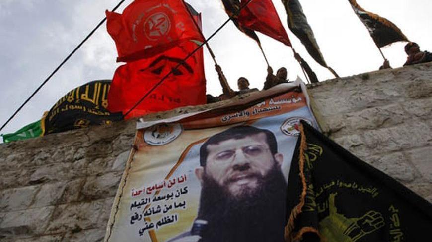 Palestinians wave flags from a wall partly covered by a banner depicting jailed Islamic Jihad leader Khader Adnan during a rally in his West Bank village of Arabeh near Jenin February 17, 2012. Several thousand Palestinians rallied in Gaza and the West Bank on Friday in support of Adnan, who is on the 62nd day of a hunger strike to protest against his detention by Israel. REUTERS/Abed Omar Qusini (WEST BANK - Tags: POLITICS CRIME LAW)