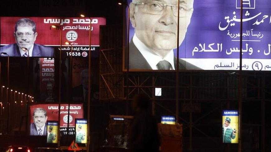 People walk under giant campaign election billboards of presidential candidates former prime minister Ahmed Shafiq (R), and Mohamed Mursi, the head of the Muslim Brotherhood's political party in Cairo May 25, 2012. Egyptians must choose between a Muslim Brother or an ex-military man in a presidential run-off that highlights the stark rifts in a nation united in euphoria when Hosni Mubarak fell 15 months ago, first-round results indicated on Friday. With most votes counted, the Muslim Brotherhood said its ca