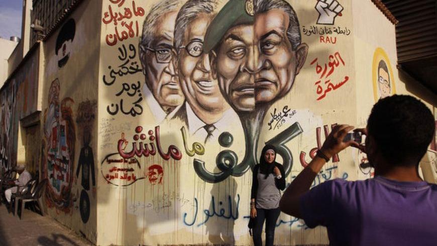 A woman gets her picture taken with a mural depicting former presidential candidate Amr Moussa (C), presidential candidate, former prime minister Ahmed Shafiq (L), and Field Marshal Mohamed Hussein Tantawi, at Tahrir Square in Cairo May 29, 2012. An attack on the offices of one of the two finalists in Egypt's presidential race has sounded a warning that the last round of voting might spark more violence in a nation polarised by the choice between Mohamed Mursi and Shafiq.  REUTERS/Ammar Awad (EGYPT - Tags: 