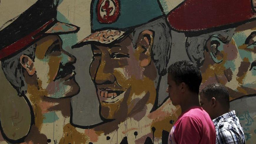 People walk in front of a wall sprayed with stencilled paintings depicting the Egyptian military council members, including Field Marshal Hussein Tantawi (C), the head of the ruling Supreme Council of the Armed Forces (SCAF), in Tahrir Square in Cairo May 24, 2012. Egypt resumes its first free presidential election on Thursday after voting passed off mostly calmly on the first day apart from a stone-throwing attack on candidate Ahmed Shafiq, who was premier for a few days before Hosni Mubarak fell. REUTERS/