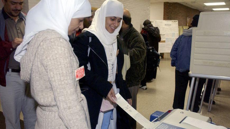 Arab-American election worker Aisha Maisari (L) watches as voter Samraa Luqman (R) casts her vote in the U.S. presidential election at a polling station in southwest Dearborn, Michigan November 2, 2004. Election workers said the lines were long all day with voters. Dearborn has one of the largest arabic speaking populations outside the Middle East. REUTERS/Rebecca Cook  RC/JDP