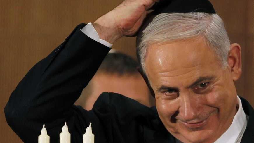 Israel's Prime Minister Benjamin Netanyahu adjusts his skull cap (yarmulke) as he lights candles for the Jewish holiday of Hanukkah after an address to the foreign media in Jerusalem December 10, 2012. REUTERS/Amir Cohen (JERUSALEM - Tags: POLITICS RELIGION)