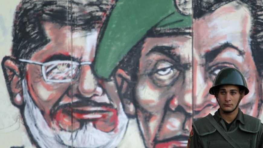 A soldier stands in front of a mural depicting Egypt's former President Hosni Mubarak (R), former Field Marshal Mohamed Hussein Tantawi (C) and Egypt's President Mohamed Mursi drawn on the wall of the presidential palace in Cairo December 12, 2012. Egypt's liberal and secular opposition said on Wednesday it would back a "no" vote in a referendum on a divisive new constitution promoted by Islamist President Mursi, calling off a boycott as long as safeguards are in place for a fair vote.   REUTERS/Khaled Abdu