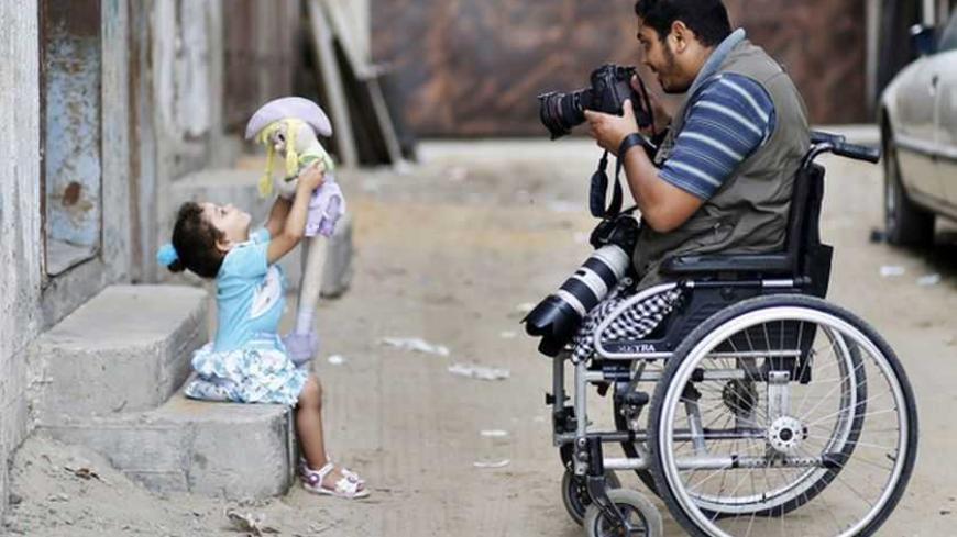 Wheelchair-bound Palestinian freelance photographer Moamen Qreiqea takes pictures of his daughter outside his home in Gaza City October 1, 2012. Qreiqea, 25, lost both his legs in an Israeli air strike in 2008 while taking pictures east of Gaza. The father of two is determined to continue his career despite his disability. REUTERS/Suhaib Salem (GAZA - Tags: MEDIA SOCIETY)