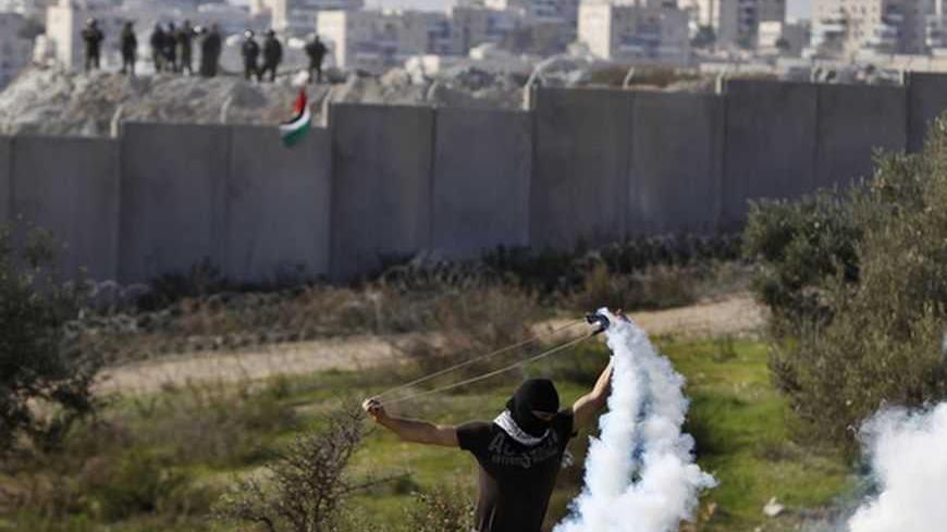 A Palestinian stone-throwing protester uses a sling to throw back a tear gas canister fired by Israeli security officers (rear) during clashes after a rally marking the 48th anniversary of the founding of the Fatah movement, in the West Bank village of Bilin near Ramallah, January 4, 2013. REUTERS/Ammar Awad (WEST BANK - Tags: POLITICS CIVIL UNREST TPX IMAGES OF THE DAY)