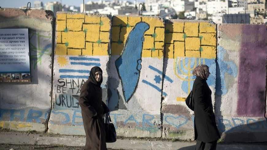 Palestinians walk past a blast wall with graffiti in the West Bank city of Hebron January 13, 2013. Entrenched in what they view as their Biblical heartland, the hardline Jewish settlers of Hebron look forward with delight to next week's Israeli election. Picture taken January 13, 2013. To match ISRAEL-ELECTION/SETTLERS   REUTERS/Baz Ratner  (WEST BANK - Tags: POLITICS ELECTIONS)