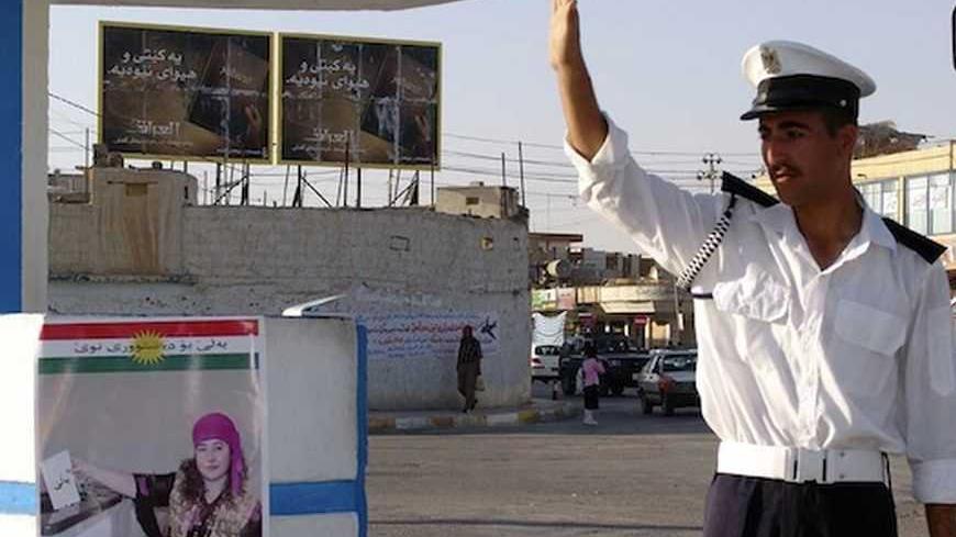 A Kurdish policeman directs traffic next to a pro-constitution poster in the northern Iraqi city of Arbil October 5, 2005. Iraq's parliament reversed itself on Wednesday over rules governing a forthcoming constitutional referendum, interpreting wording in a way that should make the October 15 ballot fairer, the assembly's acting chairman said. REUTERS/Azad Lashkari - RTR18THD