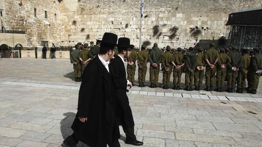 Ultra-Orthodox Jewish men walk behind Israeli soldiers at the Western Wall, Judaism's holiest prayer site, in Jerusalem's Old City February 22, 2012. The Israeli Defence Force (IDF) has always been a 'Jewish' army. Its rations are kosher, its chaplains are rabbis, and it operates - with the exception of wartime - around the festival calendar. It has never drafted soldiers from Israel's 20-percent Arab minority. But its Jewish identity has always been more cultural than religious. IDF personnel data suggests
