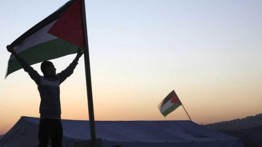 An activist holds a Palestinian flag placed near a newly-erected tent in the West Bank village of Beit Iksa, between Ramallah and Jerusalem January 20, 2013. Palestinians pitched tents in an area of the West Bank as a protest against an Israeli barrier they said would cut villagers off from their lands. The tents were erected on Friday in the Palestinian village of Beit Iksa, north of Jerusalem. REUTERS/Mohamad Torokman (WEST BANK - Tags: POLITICS) - RTR3CPAC