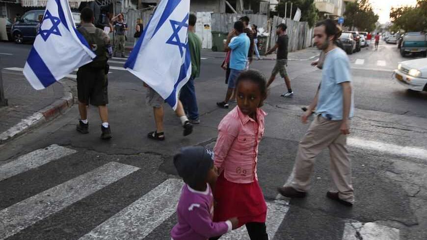 Children cross the street as residents of south Tel Aviv carry Israeli flags during a protest against African migrants living in their neighbourhoods May 30, 2012. Last week a similar protest held by residents of the low-income neighbourhoods where many of the border-jumpers from Eritrea, Sudan and South Sudan live led to violence, including a rampage that an Israeli broadcaster dubbed a "pogrom". Fleeing poverty, fighting and authoritarian rule, some 60, 000 Africans have crossed illegally into Israel thro