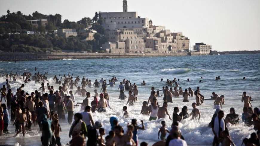 The port of Jaffa is seen in the background as Palestinians enjoy themselves at a beach in Tel Aviv during Eid al-Fitr, which marks the end of the holy month of Ramadan August 20, 2012. A spokesperson for The Israeli Coordinator for Government Activities in the Territories' (COGAT) said that improved security had allowed for the entry of over 1 million Palestinians from the occupied West Bank since the beginning of Ramadan. REUTERS/Nir Elias (ISRAEL - Tags: RELIGION SOCIETY) - RTR36ZT5