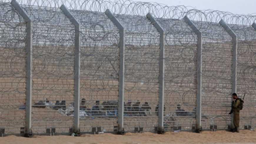 An Israeli soldier stands near the border fence between Israel and Egypt as African would-be immigrants sit on the other side near the Israeli village of Be'er Milcha September 6, 2012. Israel ruled out entry on Wednesday for 20 Africans, whom Israeli media said were from Eritrea and included at least one woman and child, who have camped on its desert border with Egypt for almost a week, part of a crackdown on migrants who walk across the porous frontier. The fence along the 260 km (160 mile)-long frontier 