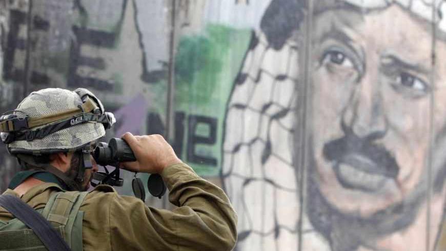 An Israeli soldier looks through binoculars in front of a mural depicting the late Palestinian leader Yasser Arafat on the controversial Israeli barrier, during clashes with Palestinian stone-throwers at Qalandiya checkpoint near the West Bank city of Ramallah November 21, 2012. Clashes broke out between Palestinians and the Israeli army in multiple locations across the occupied West Bank on Wednesday, underlining heightened tensions by the Gaza conflict. REUTERS/Marko Djurica (WEST BANK - Tags: POLITICS CI