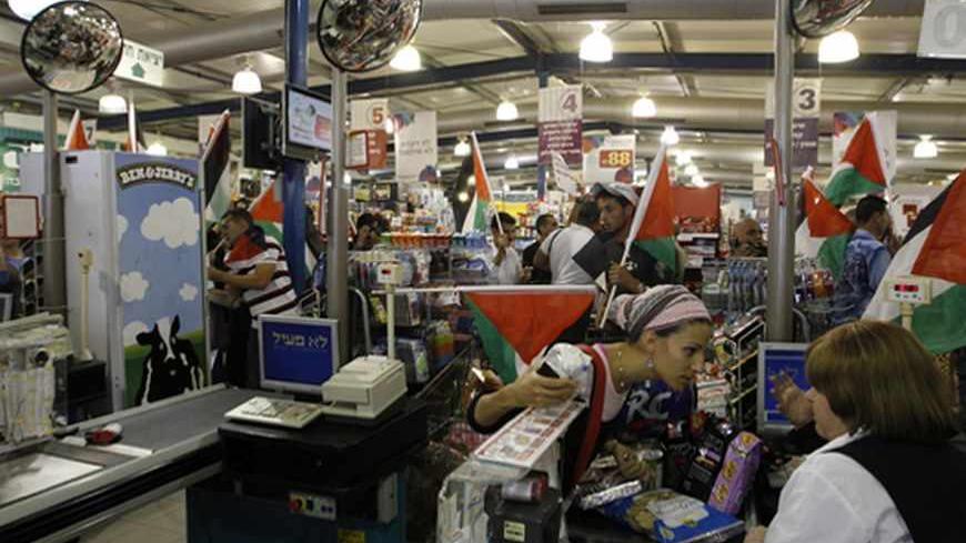 An Israeli customer speaks with a cashier as foreign and Palestinian activists holding Palestinian flags march through a supermarket in the West Bank Jewish settlement of Modiin Illit October 24, 2012. Some 50 activists marched through the supermarket and tried to block a road in the settlement on Wednesday during a protest against Jewish settlements and in a call to boycott settlement products. REUTERS/Ammar Awad (WEST BANK - Tags: POLITICS CIVIL UNREST FOOD) - RTR39INJ