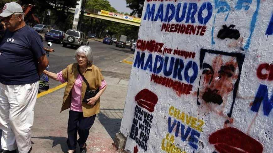 A couple walks past a wall with graffiti promoting Venezuela's acting President and presidential candidate Nicolas Maduro in Caracas April 12, 2013. The late Hugo Chavez's self-declared socialist revolution will be put to the test at a presidential election on Sunday that pits Maduro, his chosen successor against a younger rival promising change in the nation he polarized. The signs on the wall read, "Chavez forever, Maduro President" (top), "Chavez I swear to you, my vote is for Maduro" (bottom L) and "Cha